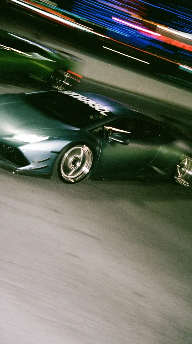 Fujifilm Portra 400H film still, 2 slammed Lamborghini Revulto with chrome wheels, in motion blur, night blur, teal & blue shadows and with purple and green glow