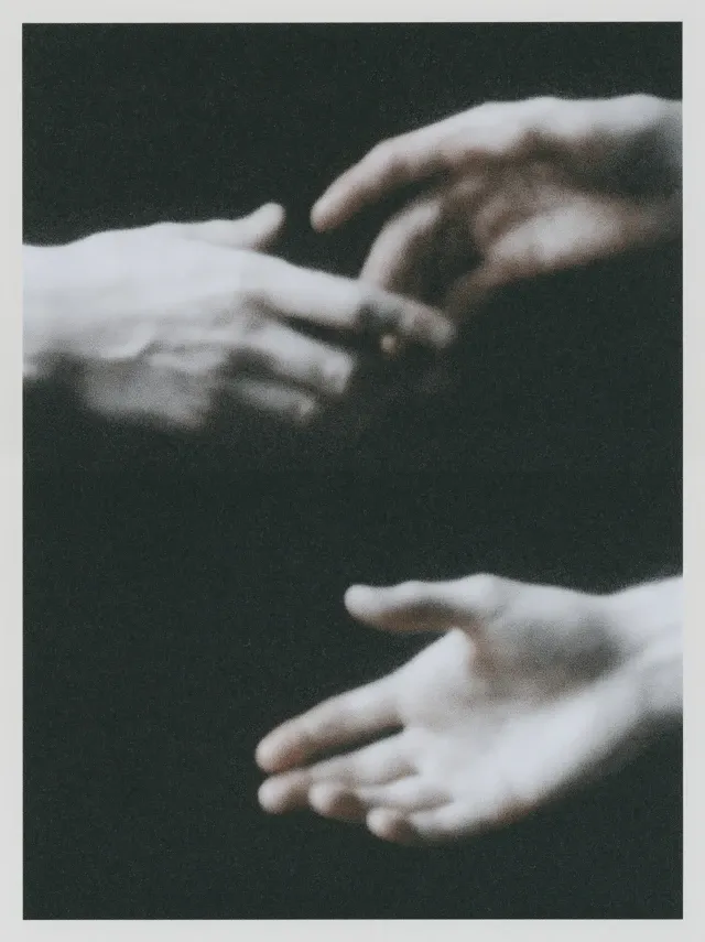 black and white photograph shacking hands, diptych of two hands reaching toward each other, fingers extended, dark background, dramatic contrast, heavy grain, analog print aesthetic, close-up, no context visible