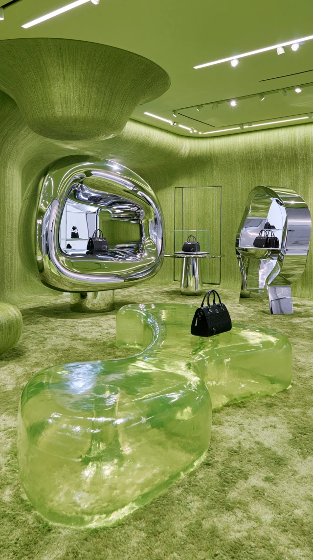 Immersive monochromatic acid chartreuse green room inside a luxury Paris Longchamp flagship, floor-to-ceiling green textile walls, thick green carpet, translucent resin furniture, sculptural mirror stainless steel displays and black handbags, surreal sophisticated fashion installation, bold but minimal, no visual clutter, gallery-quality architecture, photorealistic, 16:9