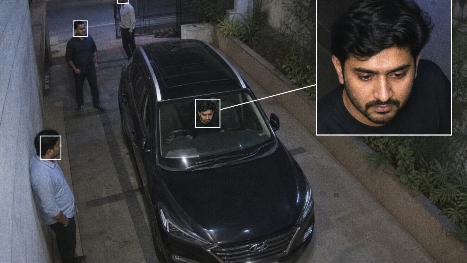 Create a high angle CCTV surveillance shot using the uploaded image as the source. Detect every visible person in the image and automatically draw a white rectangular bounding box around each face. For the most prominent person, add a large zoom in inset: a sharp, enhanced close-up of their face displayed in a floating rectangular frame connected with a thin white line.Keep the main image slightly noisy and security camera like (soft grain, slight distortion, muted colors), while the zoom in face box should be clearer, brighter, and more detailed. No text, no timestamps, no overlays except the boxes and connecting line. Maintain the original scene layout, angle, and environment of the uploaded image.